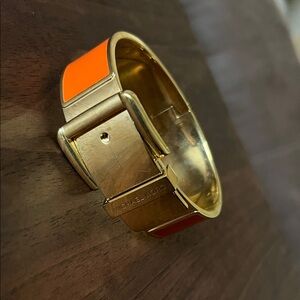 Michael Kors gold-tone and orange enamel hinged buckle bangle bracelet.